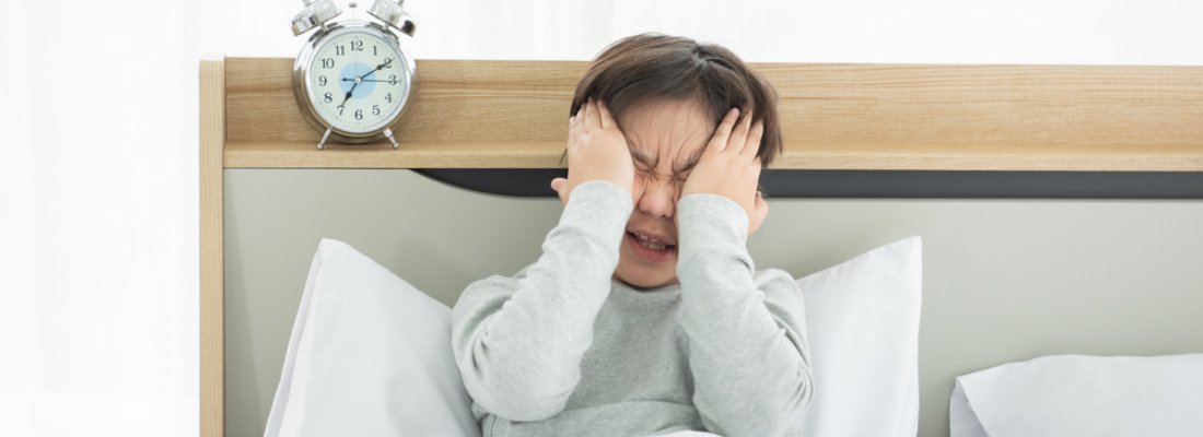 Asian boy suffering from sleep deprivation psychosis with alarm clock in bedroom